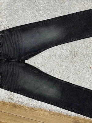 Svarta slim fit jeans med tvättade detaljer - Säljer ett par svarta slim fit jeans med snygga tvättade detaljer och lätt slitning på låren. Jeansen har klassisk femficksmodell och raka ben. Perfekta till en avslappnad streetstil. Materialet är mjukt denim i bomull.