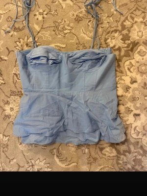 Ljusblå bustier-topp med knytband, Zara top - Supersöt ljusblå bustier-topp med tunna axelband som knyts upptill. Toppen har vadderade kupor och volangig nederdel för en romantisk vibe. Perfekt att styla med jeans eller kjol för en trendig look.