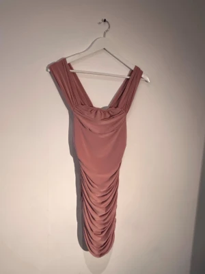 Rosa draperad kortklänning - Trendig rosa kortklänning med draperad effekt och breda axelband. Klänningen har en figurnära passform och är perfekt för dig som vill sticka ut. Tillverkad i ett mjukt och stretchigt material som ger en snygg siluett.