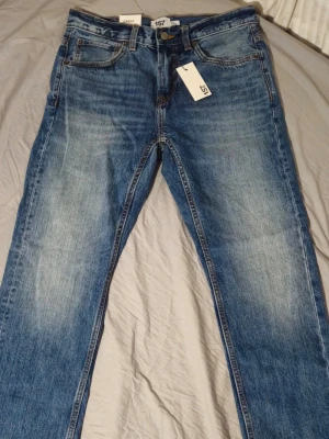 Blå clasic jeans från 157  - Snygga blå jeans från 157 med klassisk femficksmodell och raka ben. Jeansen har en lätt tvättad look med ljusare partier framtill och bak, samt gylf med dragkedja och knapp. Perfekta för en avslappnad och trendig stil. 