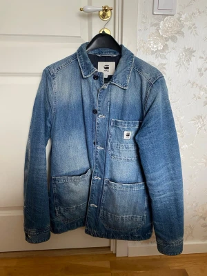 Blå jeansjacka från G-Star RAW - Snygg blå jeansjacka från G-Star RAW i klassisk modell med tre stora fickor framtill och coola slitningar. Bra skick!