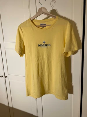 Gul Morris Stockholm T-shirt - Snygg gul t-shirt från Morris med mörkgrön  logotyp och text på bröstet. Storlek S. Skriv vid minsta fundering! 