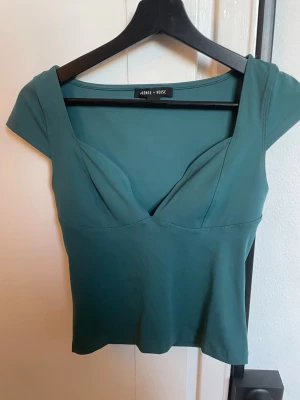 Grön topp  - Stilren grön topp från Silence + Noise/ urban outfiter med korta ärmar och v-ringad skärning. Toppens material känns mjukt och stretchigt, perfekt för en trendig look. Snygg passform som framhäver figuren och passar till många olika outfits. Köpte för 500kr endast använt 3 gånger