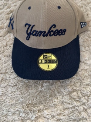 Beige Yankees keps från New Era - Snygg beige och marinblå Yankees keps från New Era 59FIFTY-kollektionen. Broderad Yankees-logga framtill, New Era-logga på sidan och flera broderade detaljer bak, inklusive 'Felti'. Klassisk rak skärm och justerbar snapback. Perfekt för dig som gillar streetwear.