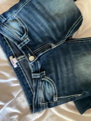 Lågmidjade jeans - Snygga blå bootcut jeans med tydliga kontrastsömmar och slitningar på låren. Klassisk femficksmodell med knapp och dragkedja. Jeansen har en cool tvättad look och är tillverkade i denim. Perfekta för dig som gillar en avslappnad men trendig stil.