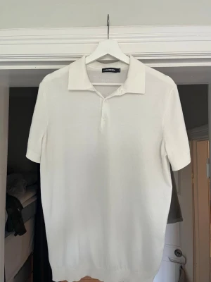 Vit stickad piké från J. Lindeberg - Vit stickad piké från J. Lindeberg med klassisk krage och korta ärmar. Toppen har två knappar framtill och är gjord i ett mjukt material som ger en clean och stilren look. Den är nästintill oanvänd och köpt på j.lindebergs butik.