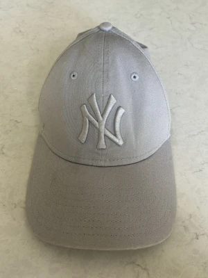 Grå New York Yankees keps New Era - Snygg grå keps från New Era med klassisk New York Yankees-logga broderad framtill. Kepsen är tillverkad i 97% bomull och 3% elastan för en bekväm passform. Perfekt accessoar för en sportig och stilren look.