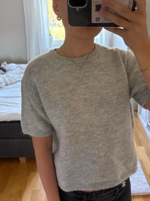 Ljusgrå stickad kort ärmad tröja  - En stilren ljusgrå stickad t-shirttröja med korta ärmar och rund halsringning. Tröjan har en rak passform och är stickad i ett mjukt material som känns skönt mot huden. Skriv om ni har frågor eller vill diskutera pris