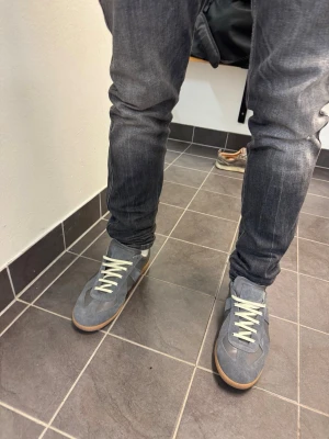 Grå sneakers från Maison margiela  - Snygga grå sneakers med vit sula och ljusa skosnören. Skorna har en klassisk låg profil och ovandel i mocka och textil. Perfekta för en avslappnad streetstil och passar till jeans eller joggers. Pris 2299 men pris går att diskuteras vid snabb affär 