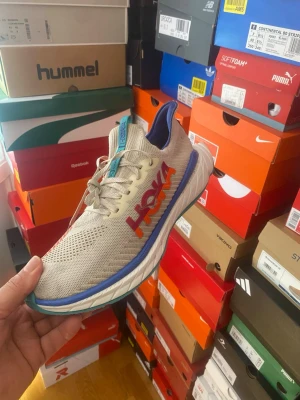 Hoka färgglada sneakers med mesh - Säljer ett par Hoka sneakers med mesh-ovandel i beige och orange, blå detaljer och lila insida. Skorna har en tjock, vit sula med blå och gröna inslag. Perfekta för dig som gillar sportig och färgstark stil.