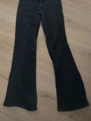 Svarta utsvängda jeans - Säljer ett par svarta jeans med utsvängda ben och klassisk femficksmodell. Jeansen har hög midja och råa kanter nertill för en cool look. Perfekta för dig som gillar retrostil och vill sticka ut lite extra.