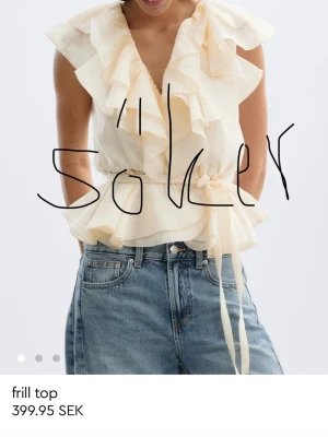 Söker i storlek S  - Supersöt ljusbeige blus med volanger och omlottknytning i midjan. Ärmlös modell med djup v-ringning och lätt transparent tyg som ger en romantisk vibe. Perfekt att styla med jeans eller kjol för en trendig look.