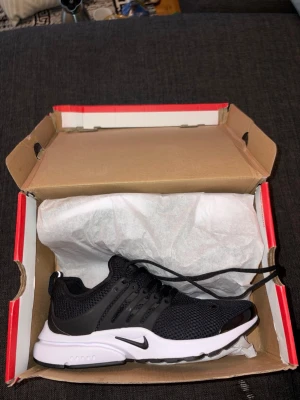 Nike Air Presto svart/vit sneaker - Nike Air Presto sneakers i svart mesh med vita och svarta detaljer. Skon har en sportig design med ventilerande ovandel, plastdetaljer vid snörningen och en vit sula med svart yttersula. Perfekt för dig som gillar stilrena och bekväma sneakers.