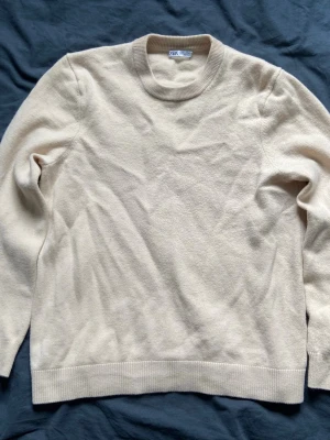 Beige stickad tröja från Zara - Klassisk beige stickad tröja från Zara med rund halsringning och ribbade muddar vid ärmslut och nederkant. Tröjan har en enkel och stilren design som passar till det mesta. Perfekt för lager på lager under kyligare dagar. Storlek m men passar mer som s!