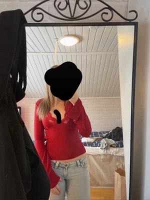 Röd långärmad topp med spets - Snygg röd långärmad topp med v-ringning och spetsdetaljer runt halsen. Modellen är figurnära och toppen har en croppad passform som ger en trendig look. Perfekt att matcha med jeans eller kjol för en cool stil.