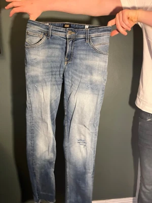 Ljusblå slitna jeans Jack & Jones - Säljer ett par ljusblå jeans från Jack & Jones med slitningar och tvättade detaljer. Modellen är smal med klassiska fem fickor och bälteshällor. Jeansen har dragkedjegylf och är tillverkade i denim med lite stretch för extra komfort.