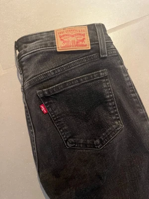 Levi's Superlow Bootcut Jeans svart - Säljer ett par svarta stentvättade Levi's Superlow Bootcut jeans med klassisk femficksdesign och röd Levi's-tag på bakfickan. Jeansen har låg midja och bootcut passform, perfekta för en avslappnad och trendig look. Tillverkade i slitstarkt denimtyg. Fint skick. Storlek 27.  300kr.
