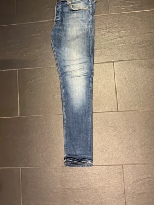 Jack and Jones jeans - Snygga blå slim fit jeans med ljusa slitningar och tvättade detaljer på låren och knäna. Klassisk femficksmodell med dragkedja och knapp. Jeansen har en smal passform och är tillverkade i stretchigt denimtyg för extra komfort. 