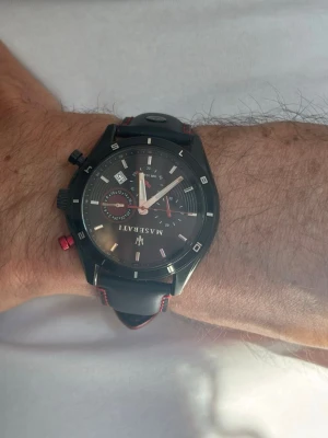 Svart Maserati kronografklocka - Stilren svart kronografklocka från Maserati med rund urtavla, vita markeringar och röda detaljer på knappar och sömmar. Klockan har datumvisning och svart läderarmband med röda sömmar. Perfekt accessoar för dig som gillar sportig och elegant stil.  Inga repor eller tecken på användning och lådan kommer med ! 
