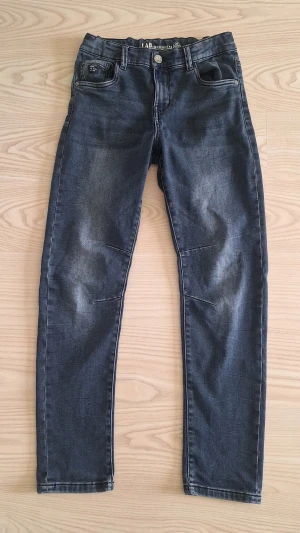 Mörkblå ungdomsjeans från LAB Industries relaxed fit stl 158 - Snygga mörkblå jeans från LAB Industries, relaxed fit modell Eddy, med klassisk femficksdesign och diskreta slitningar framtill. Jeansen har raka ben och normal midja, perfekta för en avslappnad och trendig look.