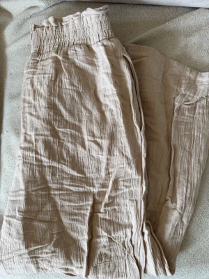 Beige vida linnebyxor med resår - Snygga och luftiga beige linnebyxor med bred resår i midjan och raka, vida ben. Byxorna har en avslappnad passform och är tillverkade i ett krinklat linnetyg som ger en chill vibe. 