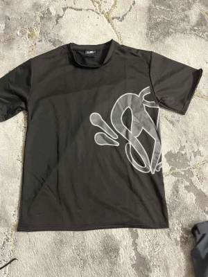 Svart t-shirt med stor grafisk print - Cool svart t-shirt från SikSilk med stor vit grafisk print både fram och bak. T-shirten har en klassisk passform med rund hals och korta ärmar. Perfekt för dig som gillar streetwear och vill sticka ut med en unik design.