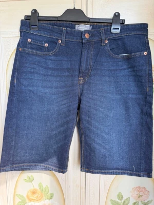 Mörkblå jeansshorts från Dressmann - Snygga mörkblå jeansshorts från Dressmann med klassisk femficksdesign och kopparfärgade nitar. Shortsen har normal passform och är tillverkade i bomull med en stilren look. 