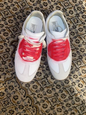 Maison margiela gats japan - Maison Margiela sneakers i vitt läder med röda spraydetaljer och vita mockapartier. Klassisk låg modell med gummisula och vita samt rosa skosnören. Ikonisk design med en edgy twist, perfekt för dig som vill sticka ut. Box medföljs. Köpta för 3900