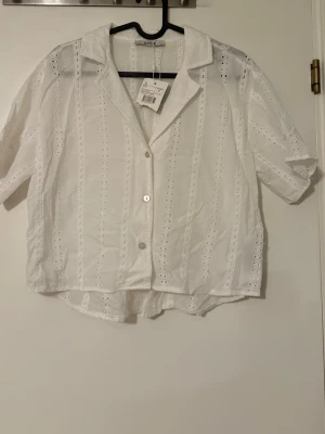 Vit broderad croppad skjorta med kort ärm - Vit skjorta från Koton med broderade detaljer och korta ärmar. Skjortan har knappar framtill, krage och ett luftigt loose fit. Perfekt för en fräsch och stilren look.
