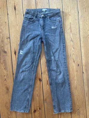 Grå/ svarta jeans med slitningar - Säljer ett par grå jeans med raka ben och slitningar på låret och knät. Lite slitningar längst ner pga användning annars bra skick. Från Gina Young storlek 164