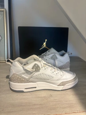 Vita Air Jordan sneakers med grå detaljer - Säljer ett par vita Air Jordan sneakers med grå detaljer och mönstrad häl. Skorna har meshpaneler på sidorna, klassisk snörning och en hög siluett. Perfekta för dig som gillar streetwear och vill ha en clean look.