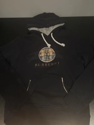 Navy Burberry hoodie med logga - Snygg navy hoodie från Burberry med klassisk rutmönstrad logga på bröstet och vit dragsko i huvan. Mjuk insida och stor magficka framtill. Hör av dig vid intresse!