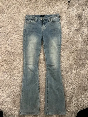 Bootcut jeans från True Religion - Ljusblå bootcut jeans från True Religion med klassiska fem fickor och snygga detaljer på bakfickorna. Använda bara ett fåtal gånger eftersom de är för stora.