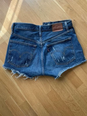 Levi's blå jeansshorts med fransar - Säljer ett par klassiska blå jeansshorts från Levi's med råa fransade kanter och femficksmodell. Shortsen har hög midja men de är jätte snygga nedvikta om man vi ha dem lite mer lågmidjat. 