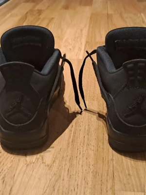 Svarta Air Jordan 4 Retro sneakers - Snygga helsvarta Air Jordan 4 Retro sneakers med klassisk siluett och ikoniska Jumpman-loggan på hälen. Skorna har ovandel i mocka och mesh, samt tjock sula för extra komfort. Perfekta för dig som gillar streetwear och vill ha en stilren look.