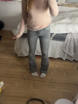 Grå bootcut jeans med låg midja - Säljer ett par gråa bootcut jeans med låg midja och klassisk femficksdesign. Jeansen har en snygg passform som framhäver benen och är perfekta för dig som gillar en avslappnad men trendig stil. Materialet är denim och färgen är ljusgrå.