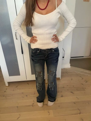 Mörkblå slitna bootcut jeans - Snygga mörkblå bootcut jeans med slitningar och hål på både fram- och baksida av benen. Jeansen har klassisk femficksdesign och låg midja. Perfekta för en avslappnad och trendig look.