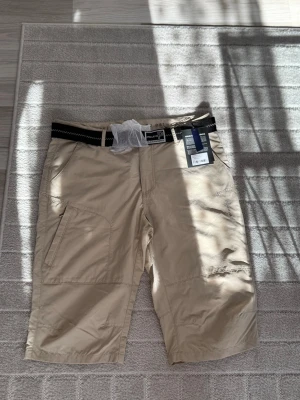 Beiga shorts med bälte från PELLE P - Snygga beiga shorts från PELLE P med praktiska fickor och svart bälte med vita detaljer. Perfekta för varma dagar och har en avslappnad passform. Tillverkade i ett lätt och slitstarkt material som känns bekvämt hela dagen.