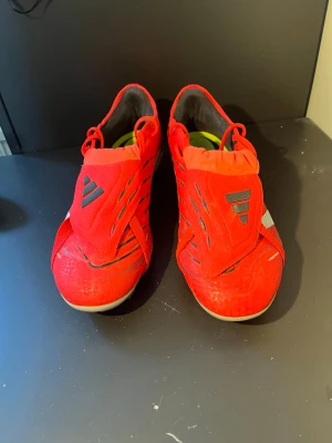 Adidas Predator röda fotbollsskor - Använda 2 gånger. Nypris 2100kr.Säljer ett par röda Adidas Predator fotbollsskor med vita och svarta detaljer. Skorna har klassisk snörning, täckt plös och mönstrad ovandel för extra grepp. Snygg design med tre vita ränder på sidan och dobbar för spel på gräsplan.