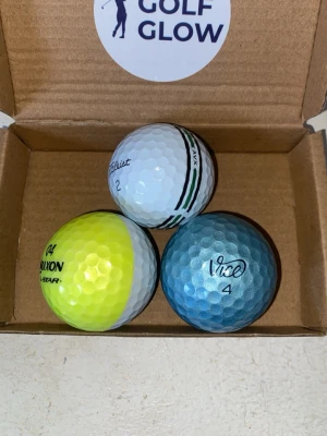 En Srixon device, en vice pro plus (blå) och en titlest AVX stripe  - Säljer tre golfbollar: en vit Titleist med gröna detaljer, en gul/vit Srixon och en blå Vice. Alla bollar har klassisk dimple-yta och är tillverkade i slitstarkt material. Perfekt för dig som vill testa olika märken på banan.