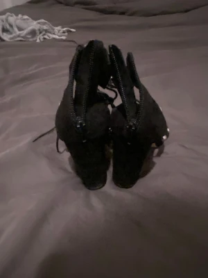 Svarta pumps med nitar och snörning - Säljer ett par svarta pumps med chunky klack, dekorerade med silvriga nitar och snörning framtill. Skorna har dragkedja bak för enkel påtagning och är i mockaliknande material. Perfekta för dig som vill sticka ut med en edgy stil.