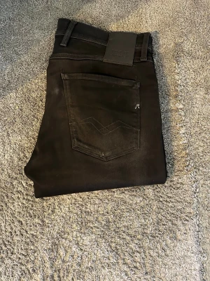 Svarta jeans från Replay - Snygga svarta jeans från Replay med klassisk femficksdesign och diskreta sömdetaljer på bakfickan. Jeansen har normal midja och dragkedjegylf. Perfekta för en stilren och modern look. Riktigt fräscha och inte använda mycket. Ställ gärna frågor!😃