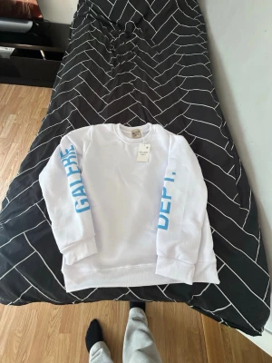 Vit sweatshirt från Gallery Dept. – storlek M – helt ny med prislapp - Säljer en stilren vit sweatshirt från Gallery Dept. i storlek M. Tröjan är helt ny och oanvänd, med original prislapp kvar. Modern design med blått tryck på ärmarna och ryggen som ger ett snyggt och trendigt uttryck.  Perfekt för både vardag och streetwear-look. Observera att påse ej medföljer. Priset kan diskuter   Hör av dig vid frågor eller intresse!