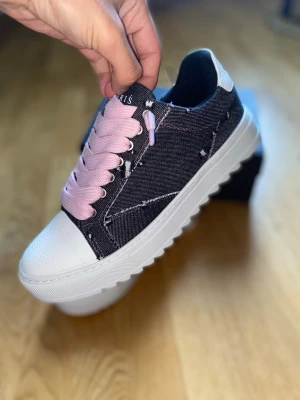 Numeriś Pink Denim - denim med slitna detaljer, breda rosa skosnören och vit, chunky sula. Tåpartiet är i vitt läderliknande material och skon har en modern streetstyle-vibe. Perfekta för dig som vill sticka ut med din stil.