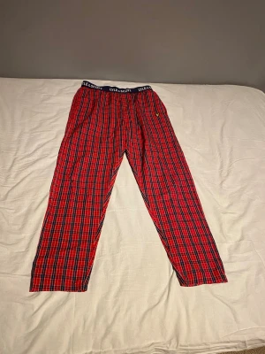 Rödrutiga pyjamasbyxor Lyle & Scott - Snygga rödrutiga pyjamasbyxor från Lyle & Scott med klassiskt tartanmönster. Byxorna har resår i midjan med logotyp och är tillverkade i mjukt tyg, perfekta för att chilla hemma. Liten gul logga broderad på ena benet.