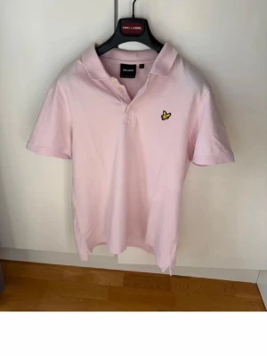 Lyle & Scott Piké  - Säljer en ljusrosa pikétröja från Lyle & Scott med klassisk krage och två knappar framtill. Tröjan har korta ärmar och den ikoniska gula loggan broderad på bröstet. Tillverkad i mjuk bomull för en skön känsla. 🎉SlimFit 🎉För mer info skriv dm!