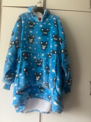 Blå oversized hoodie med koalamotiv - Supermjuk och oversized blå hoodie med gulliga koalor och moln över hela plagget. Har stor ficka framtill, huva och fluffigt vitt foder på insidan. Perfekt för mysiga hemmakvällar eller när du vill vara extra bekväm.