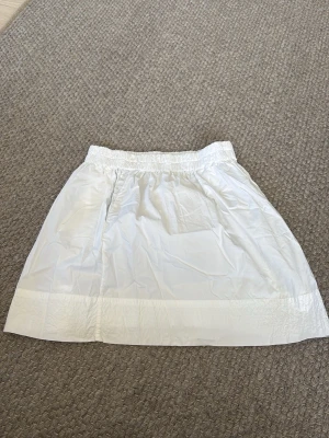 Vit kortkjol med resårmidja - Säljer en vit kortkjol med resår i midjan. Kjolen har enkel design och är tillverkad i ett lätt material som känns bekvämt. Perfekt för dig som gillar en clean och stilren look.