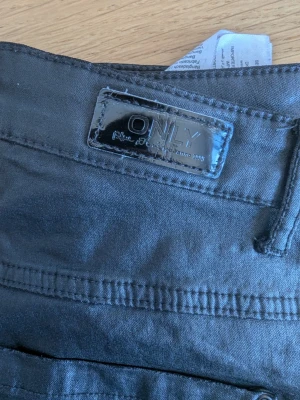 Svarta skinny skinn  jeans från ONLY - Säljer ett par svarta skinny skinn/läder jeans från ONLY med klassisk femficksdesign och snyggt lädermärke bak. Jeansen har smal passform och är tillverkade i ett stretchigt material som sitter bekvämt. Perfekta för dig som gillar en stilren look.