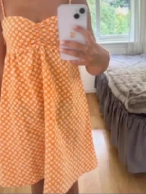 Gul blommig kortklänning med smala axelband - Söt gul kortklänning med vita blommor och smala axelband. Klänningen har en lätt A-linjeform och är perfekt för varma dagar. Materialet känns lätt och luftigt, och den har en enkel, ungdomlig design som är superfräsch.